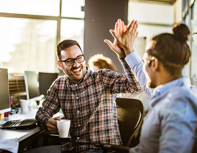 Two happy employees high fiving at the work desk