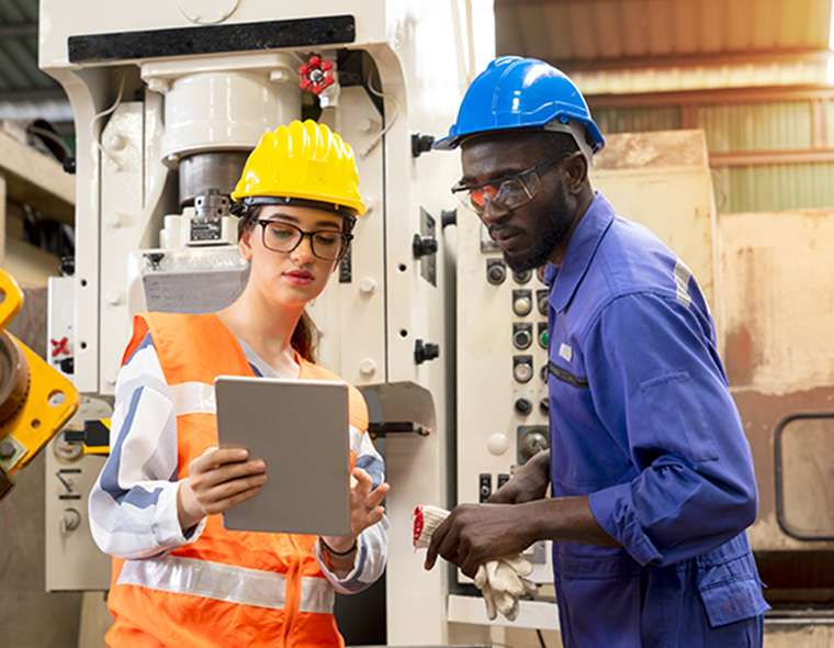 Two workers in safety equipment looking at tablet in manufacturing facility